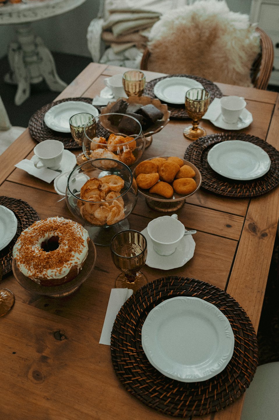 Rustic wooden table set with pastries and teacups for a meal.