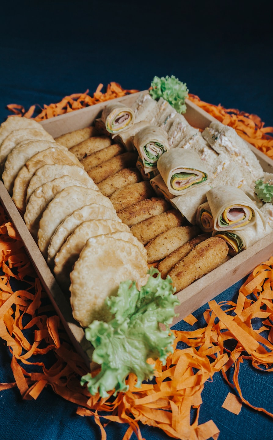 Wooden tray of assorted savory snacks and finger sandwiches.