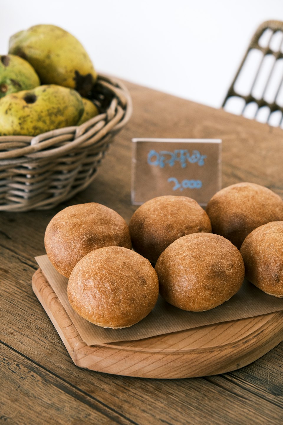 Six freshly baked bread rolls sit on a wooden table.