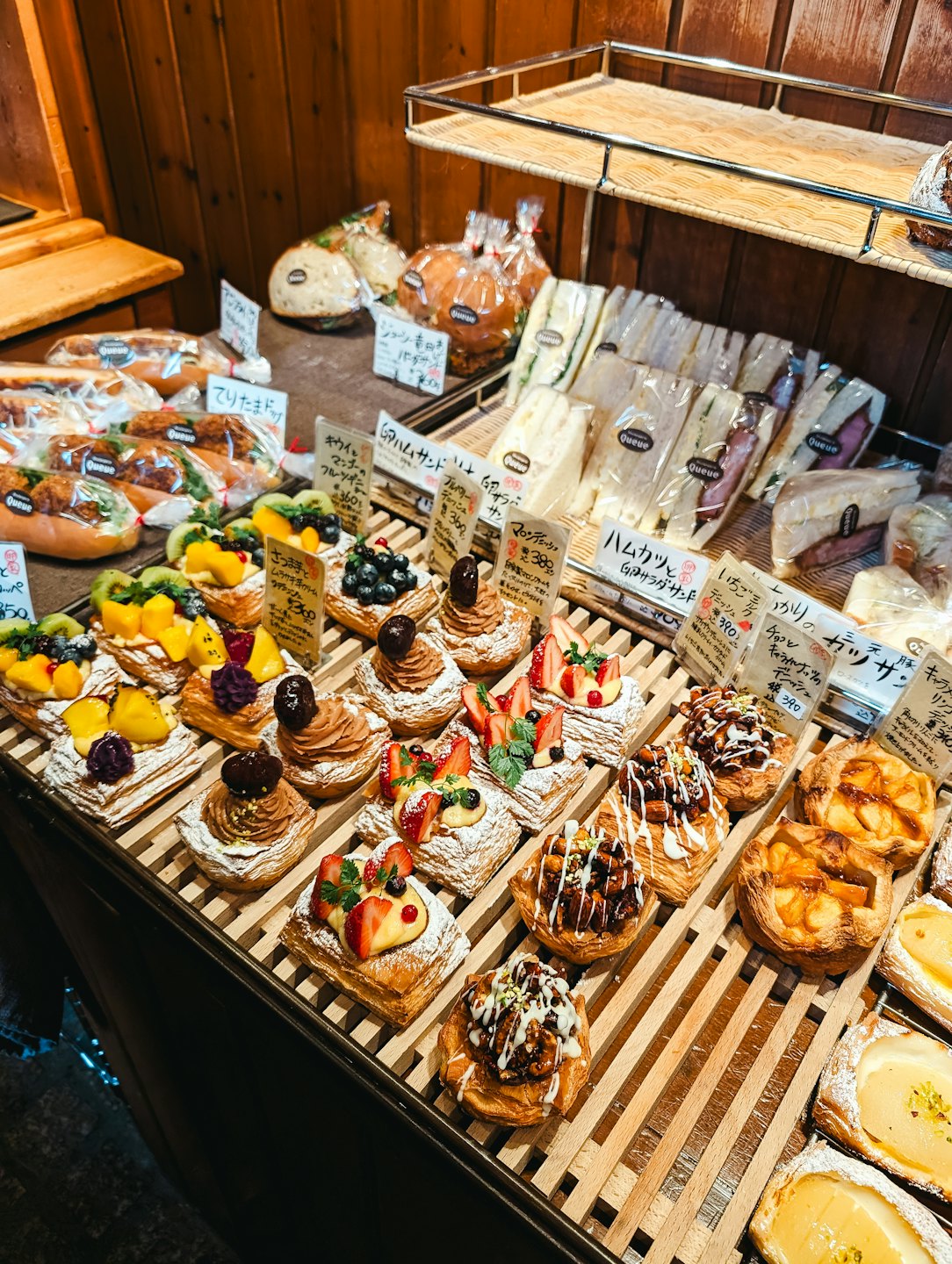 Freshly baked pastries and sandwiches displayed on wooden bakery shelves.